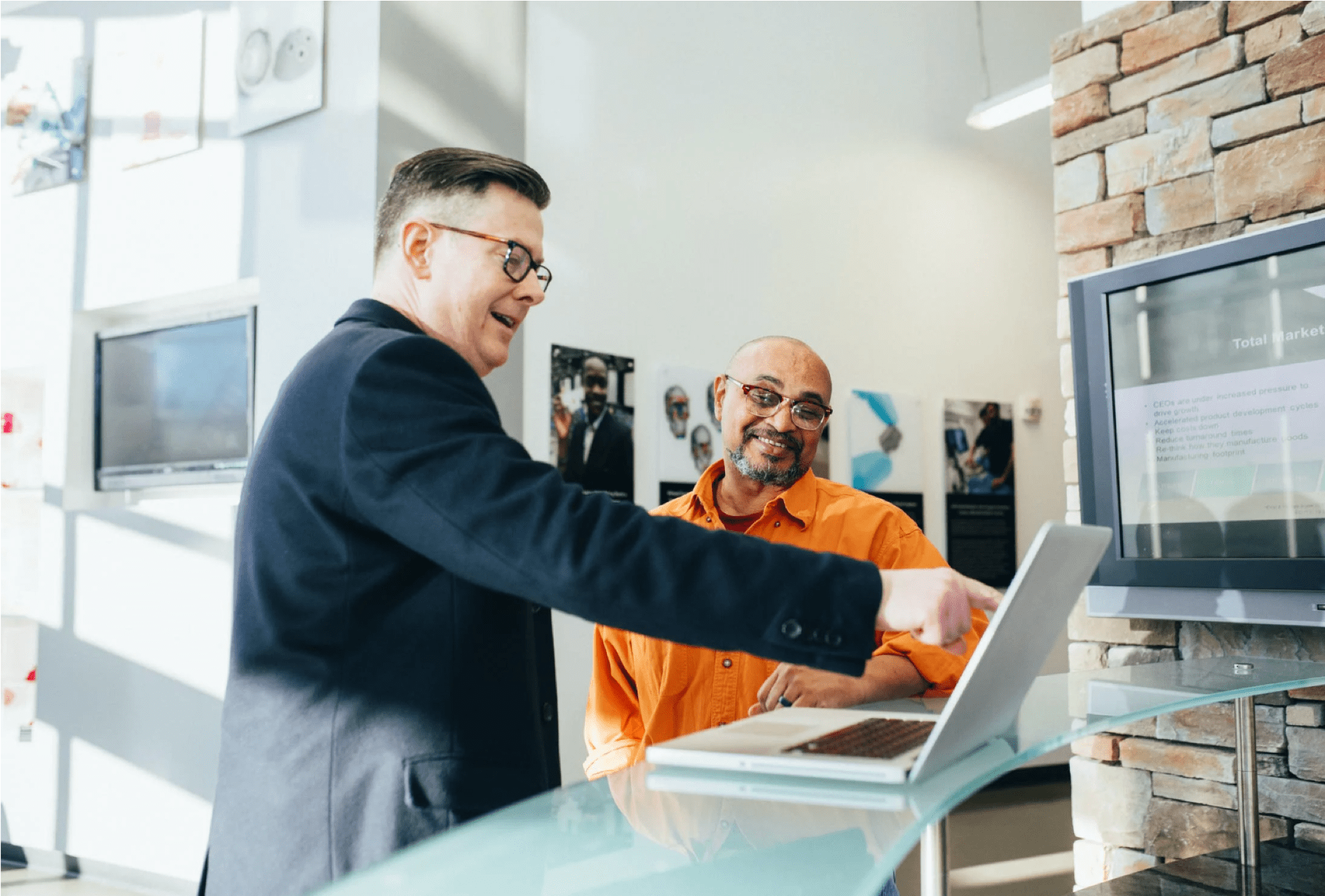 a person in a suit showing a person in an orange shirt something on a laptop screen